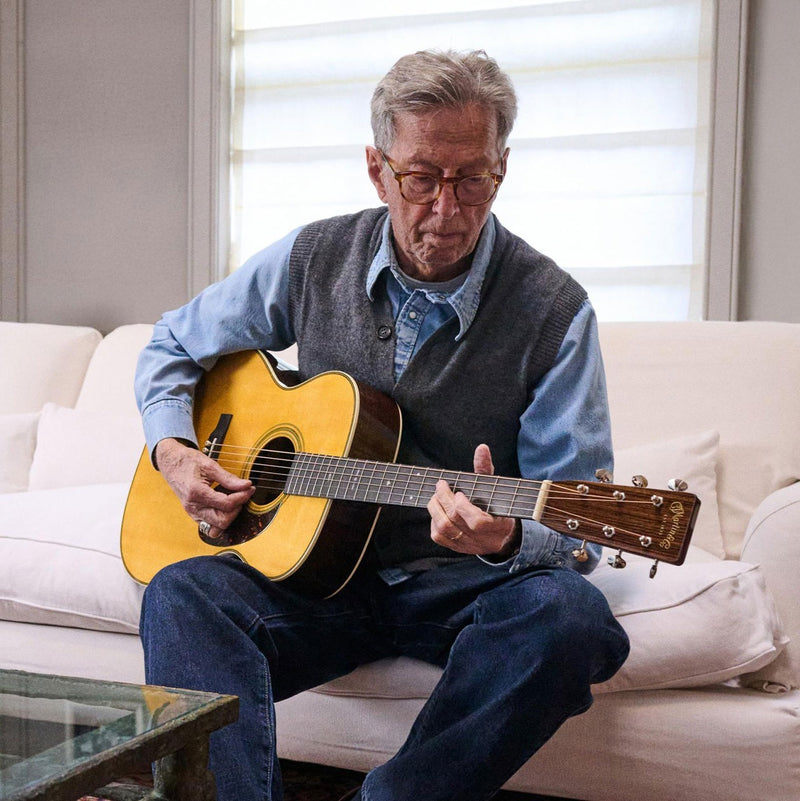 Eric Clapton playing a Martin acoustic guitar on a couch in Martin’s anniversary photography
